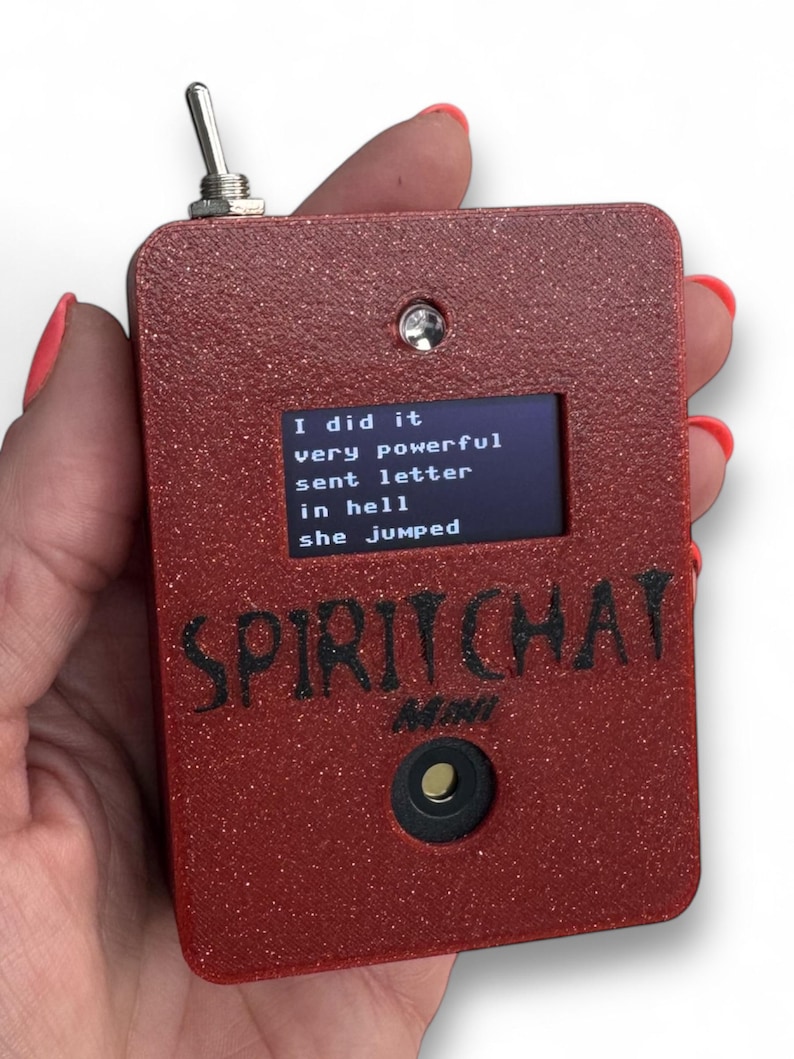 May include: A rectangular red glittery electronic device labeled SPIRIT CHAT MINI with a toggle switch on top, a small screen displaying the text I did it very powerful sent letter in hell she jumped, and a circular button below the text.