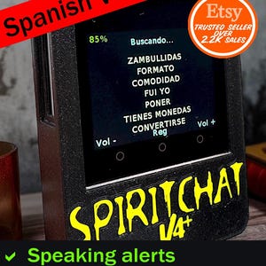 May include: A black electronic device with a screen displaying text in Spanish. The device has the words "SPIRITCHAT V4+" in yellow, and the text "Speaking alerts" and "Magnetometer Trigger" in green. An Etsy trusted seller badge is visible.