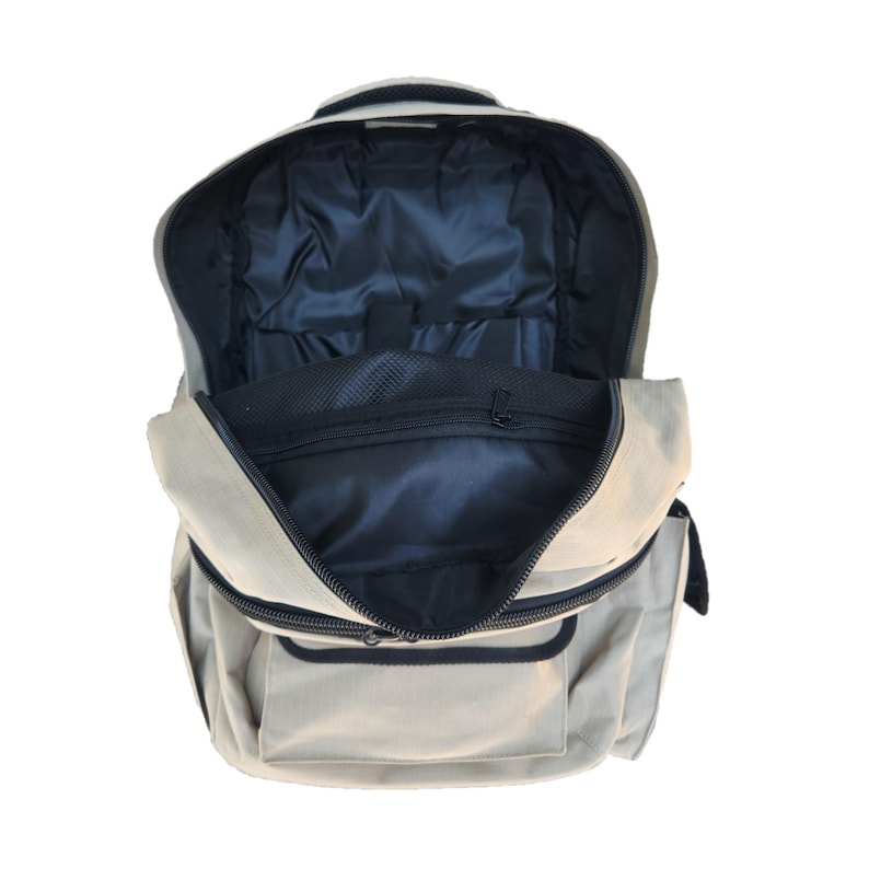 Puede incluir: Una mochila de lona beige con una cremallera negra y un bolsillo de malla negra en el interior. La mochila est&aacute; abierta y el interior es visible.