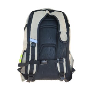 Puede incluir: Una mochila de lona beige con correas negras y un panel trasero de malla. La mochila tiene un peque&ntilde;o bolsillo en la parte delantera y una tira reflectante en el lateral.