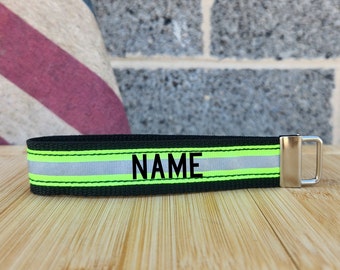 May include: Black and green key chain with a reflective strip and the word "NAME" embroidered in black.