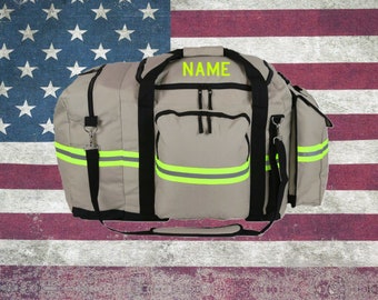 May include: A large, gray duffel bag with black straps and a yellow reflective stripe. The bag has a zippered pocket on the front and the word "NAME" embroidered in yellow on the top.