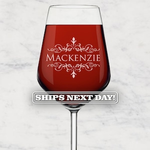 May include: A stemmed wine glass filled with red liquid. The glass has a clear bowl and a long, slender stem. The word "Mackenzie" is displayed in white script with decorative flourishes. The text "SHIPS NEXT DAY!" is displayed on a banner.