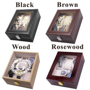 May include: Four watch display cases in black, brown, wood, and rosewood. Each case has a glass top, a silver clasp, and a light-colored interior. The black case has the name "Miller" and the letter "M". The brown case has the name "Henry" and the letter "H". The wood case has the letter "G" and a laurel wreath. The rosewood case has the name "Henry" and the letter "H".