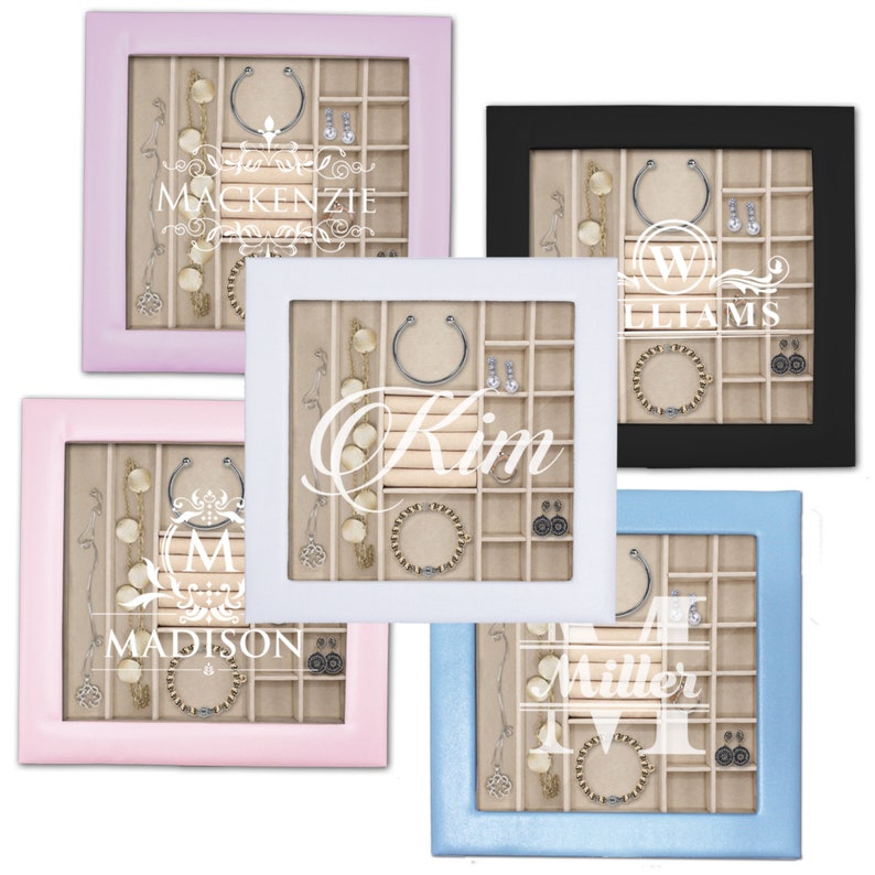 May include: Five square jewelry display cases with glass lids, featuring frames in light pink, black, white, soft pink, and light blue. Each case has a beige interior with multiple compartments containing necklaces, bracelets, and earrings.