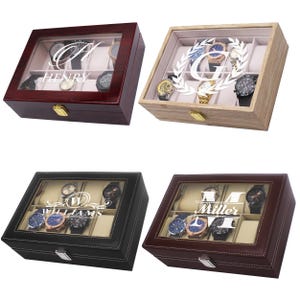 May include: Four watch display cases in various colors: dark red, light wood, black, and brown. Each case has a glass top, a name or initial design, and a gold-colored clasp. The cases hold multiple watches.
