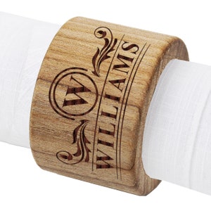 May include: Wooden napkin ring with a personalised engraved design. The ring features a decorative scroll design with the initial "W" in a circle and the name "WILLIAMS" engraved below.