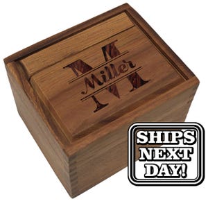 May include: A square wooden box with a lid featuring a laser-engraved design of a large letter M, the name Miller, and the letter M below it. The box has visible finger joints at the corners and a natural brown wood grain finish throughout.