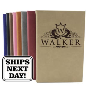 May include: A collection of rectangular journals with smooth covers in various colors including tan, maroon, gray, brown, pink, black, and blue. The tan journal in the foreground features a dark brown crest logo with the letter W and the name WALKER.