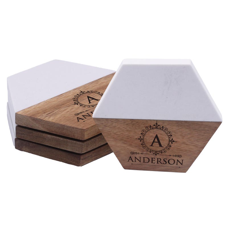 Puede incluir: Una pila de posavasos hexagonales con un dise&ntilde;o dividido en material blanco y madera marr&oacute;n natural. Cada posavasos est&aacute; grabado con un emblema circular decorativo que contiene la letra A y el texto ANDERSON centrado debajo.