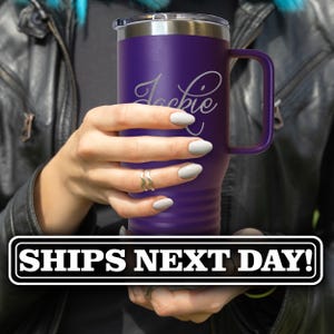 May include: A purple stainless steel tumbler with a handle and a clear lid. The tumbler features a matte finish and is engraved with the name Jackie in a cursive script font. The body of the tumbler has horizontal ridges near the base.