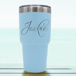 May include: A light blue stainless steel tumbler with a black inscription that reads "Jackie" in a cursive font.