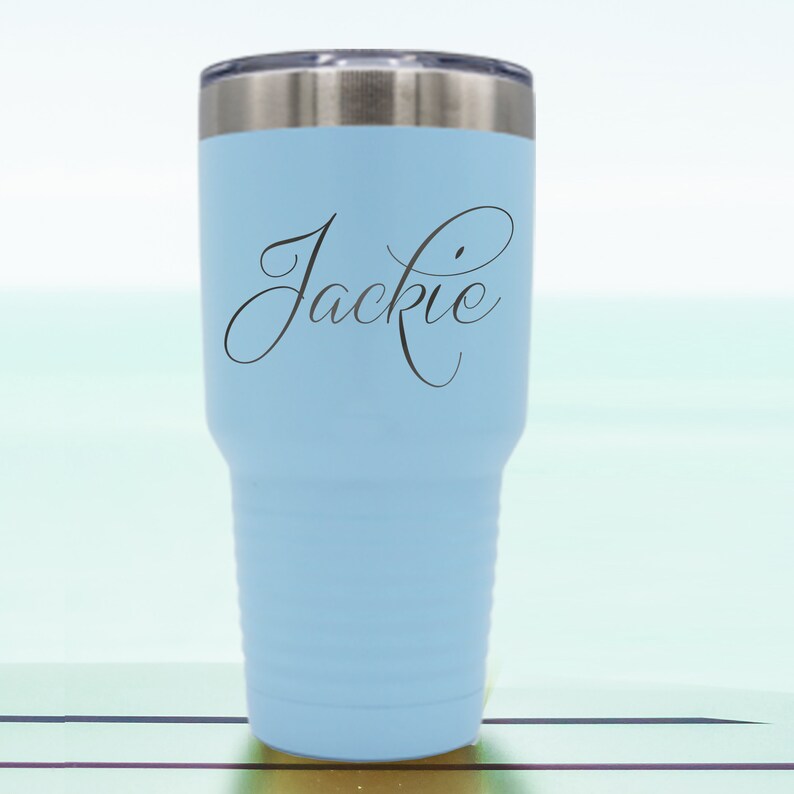 May include: A light blue stainless steel tumbler with a black inscription that reads "Jackie" in a cursive font.