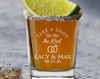 May include: A shot glass with a salted rim, filled with a golden liquid, and topped with a lime wedge. The glass is etched with the words "TAKE A SHOT, We Tied the Knot", two wedding rings, and the names "LACY & MAX" with the date "08-27-26".