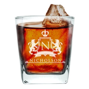 May include: A square, clear glass with a personalized design. The design features a crown, a shield with the letter "N", and two lions. The text "NICHOLSON" is below the shield. The glass is filled with a dark liquid and ice.