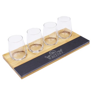 May include: A wooden serving tray with four stemless wine glasses. The tray has a bamboo base with a black slate accent. The slate is engraved with the name "WHITNEY" and a stylized "W" initial.