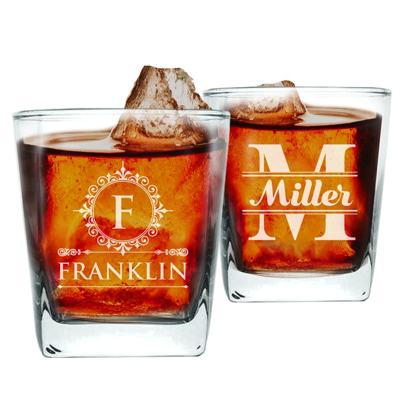 May include: Two clear glass whiskey glasses with a personalized design. The glass on the left has the letter "F" in a decorative frame and the word "FRANKLIN" below. The glass on the right has the letter "M" in a decorative frame and the word "Miller" below.