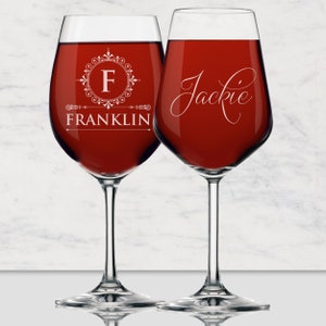 May include: Two clear glass wine glasses filled with deep red liquid. The left glass features a white circular filigree emblem with the letter F and the name FRANKLIN below. The right glass displays the name Jackie in a white cursive script font.