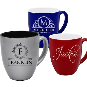 May include: Three ceramic mugs in blue, silver, and red. The blue mug has a white monogram with the name "Meredith". The silver mug has a monogram with the name "Franklin". The red mug has the name "Jackie" in script.