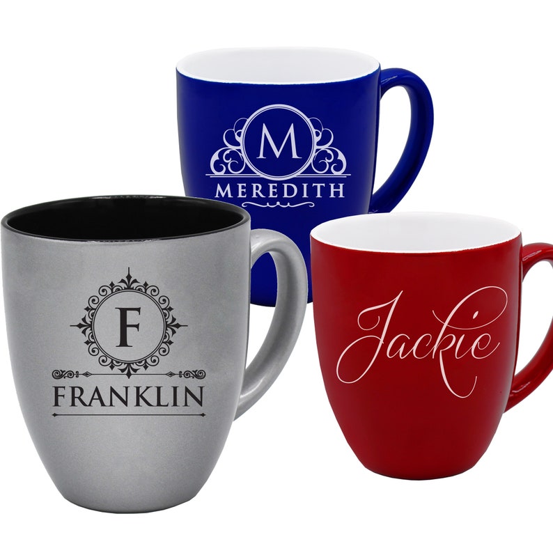 May include: Three ceramic mugs in blue, silver, and red. The blue mug has a white monogram with the name "Meredith". The silver mug has a monogram with the name "Franklin". The red mug has the name "Jackie" in script.