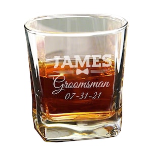 Może przedstawiać: Przezroczysty szklany kieliszek do whisky z wygrawerowanym imieniem "JAMES" z przodu, a także słowem "Groomsman" i datą "07-31-21".