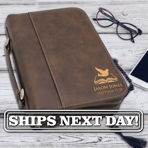 May include: A brown faux leather Bible cover with a handle and a zipper closure. The cover features an engraved graphic of a dove flying over an open book, with the text JASON JONES and MATTHEW 11:28 engraved below the graphic on the front panel.