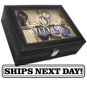 May include: Black leather watch box with a clear glass top, white stitching, and a silver clasp. The box contains several watches and the name "WILLIAMS" is displayed on the glass. The box is designed to hold multiple watches.