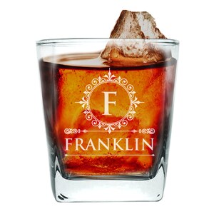 Op de afbeelding: Een vierkant, helder glas met een gegraveerd monogram. Het glas is gevuld met een donkerbruine vloeistof en ijs. Het monogram heeft een decoratieve versiering en de letter "F" met de naam "FRANKLIN" eronder.