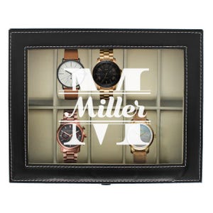 May include: A black leather watch box with a clear top, holding four watches. The watches have brown, gold, and rose gold tones. The box has the name "Miller" in white lettering.