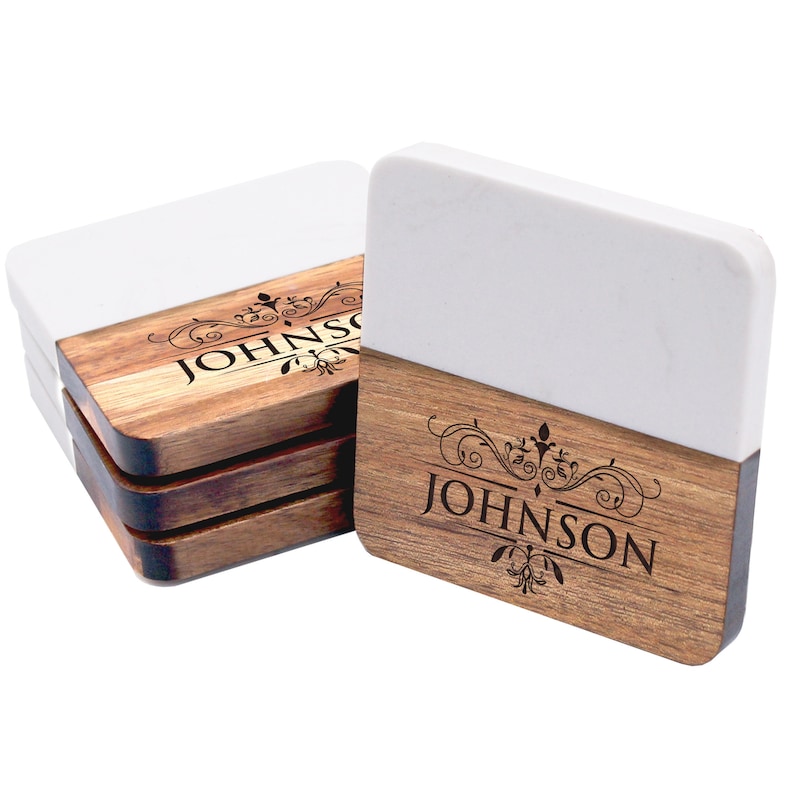 Puede incluir: Un juego de posavasos cuadrados con un dise&ntilde;o bicolor que combina una secci&oacute;n superior blanca lisa y una secci&oacute;n inferior de madera natural. Cada posavasos est&aacute; grabado con el nombre JOHNSON en may&uacute;sculas y motivos decorativos.