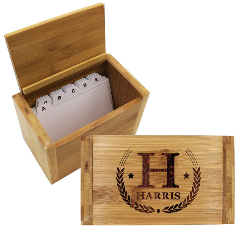 Puede incluir: Una caja de recetas rectangular de bamb&uacute; con tapa abatible que presenta un dise&ntilde;o grabado con l&aacute;ser de la letra H, el nombre HARRIS, dos estrellas y una corona de laurel. La caja abierta contiene fichas blancas con pesta&ntilde;as de la A a la E.