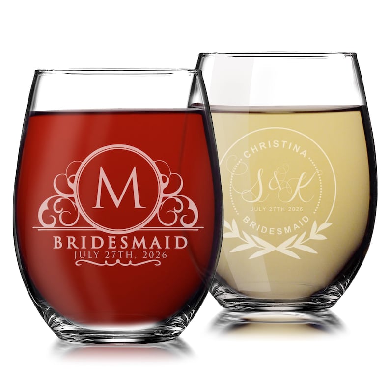 May include: Two stemless wine glasses with etched designs. The left glass contains red liquid and features a letter M inside a circle with the text BRIDESMAID and JULY 27TH, 2026. The right glass contains white liquid with a circular design, the name CHRISTINA, the initials S&K, and the text JULY 27TH, 2026 and BRIDESMAID.