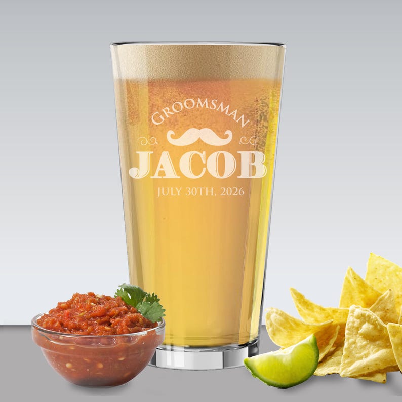 May include: A pint glass filled with beer, featuring the text "Groomsman JACOB JULY 30TH, 2026" and a mustache graphic. A small bowl of salsa, tortilla chips, and a lime wedge are in the foreground.