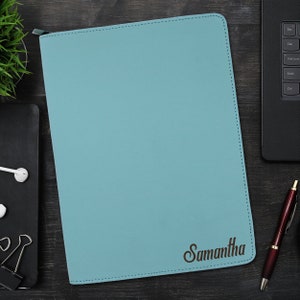 May include: A rectangular, light blue zipped portfolio case with rounded corners and visible stitching along the edges. The name Samantha is engraved in a dark brown script font in the bottom right corner of the front cover.