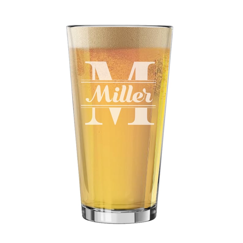 May include: A clear pint glass filled with beer and foam. The glass has a silver rim and features the name "Miller" with a large "M" etched into the glass. The beer is a light amber color.