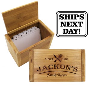 Puede incluir: Una caja de recetas rectangular de bamb&uacute; con la tapa abierta y divisores alfab&eacute;ticos blancos en el interior. La tapa presenta un dise&ntilde;o grabado con un cuchillo y un tenedor cruzados, el texto "SINCE 1985", "JACKON'S" y "Family Recipes".