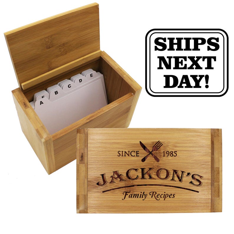 Puede incluir: Una caja de recetas rectangular de bamb&uacute; con la tapa abierta y divisores alfab&eacute;ticos blancos en el interior. La tapa presenta un dise&ntilde;o grabado con un cuchillo y un tenedor cruzados, el texto "SINCE 1985", "JACKON'S" y "Family Recipes".