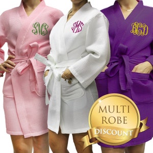 May include: Three waffle weave robes in pink, white, and purple with personalized monograms. The robes have a sash tie and pockets. The text "MULTI ROBE DISCOUNT" is on a gold circle with a gold ribbon.