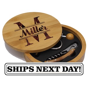 May include: A round bamboo wine accessory box with a lid featuring the engraved text Miller and a large letter M. The interior contains a metal corkscrew with a wooden handle, a metal wine ring, and a small wooden stopper set in black foam.