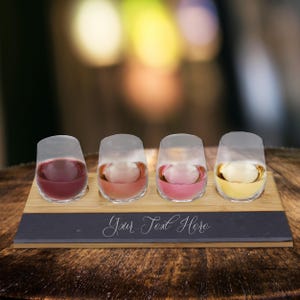 May include: A wooden serving tray with four stemless wine glasses, each filled with a different colored wine. The tray has a dark gray slate insert with the text "Your Text Here" in cursive.