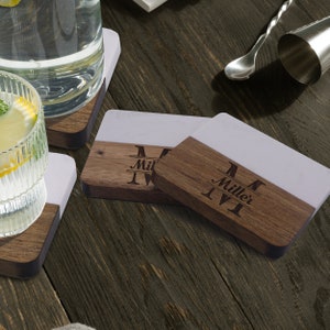 Puede incluir: Posavasos rectangulares con un dise&ntilde;o bicolor que combina una superficie de m&aacute;rmol blanco liso y una base de madera marr&oacute;n oscura. La secci&oacute;n de madera est&aacute; grabada con una letra M grande, el nombre Miller y otra M en estilo monograma.