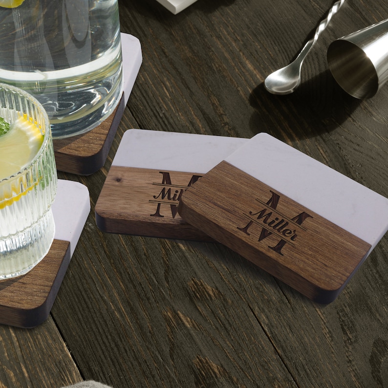 Puede incluir: Posavasos rectangulares con un dise&ntilde;o bicolor que combina una superficie de m&aacute;rmol blanco liso y una base de madera marr&oacute;n oscura. La secci&oacute;n de madera est&aacute; grabada con una letra M grande, el nombre Miller y otra M en estilo monograma.