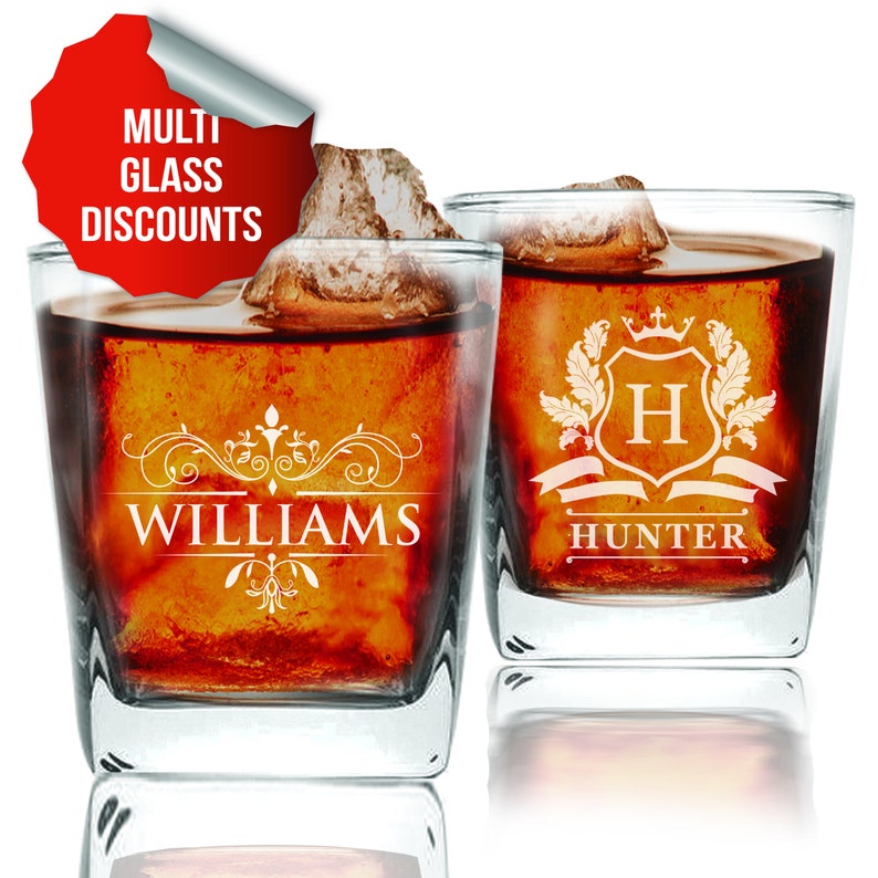 May include: Two clear glass tumblers with personalized engravings. The tumbler on the left has the name "WILLIAMS" with a decorative design. The tumbler on the right has a crest with the letter "H" and the name "HUNTER".