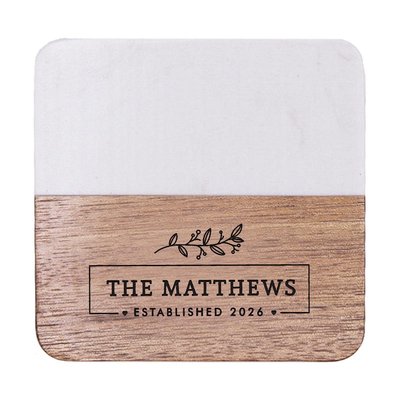 Puede incluir: Un posavasos cuadrado con una mitad superior de m&aacute;rmol blanco y una mitad inferior de madera natural. La secci&oacute;n de madera est&aacute; grabada con un gr&aacute;fico bot&aacute;nico negro, el texto THE MATTHEWS y ESTABLISHED 2026 junto a dos peque&ntilde;os corazones.