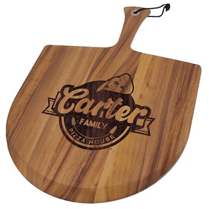 Peut inclure: Une pelle &agrave; pizza en bois avec une poign&eacute;e et une surface plate et arrondie. La pelle porte l'inscription grav&eacute;e "Carter Family Pizza House" avec un dessin de part de pizza. Un cordon noir est attach&eacute; &agrave; la poign&eacute;e.