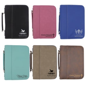 May include: A collection of six personalized Bible covers in various colors: black, pink, blue, teal, taupe, and brown. Each cover features a handle, a zipper closure, and custom text with a name and Bible verse. The covers have a dove or cross design.