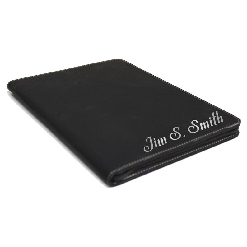 May include: A rectangular black portfolio case with visible stitching along the edges. The front surface features the engraved name Jim S. Smith in a cursive script font. The item is positioned at an angle against a plain white background.