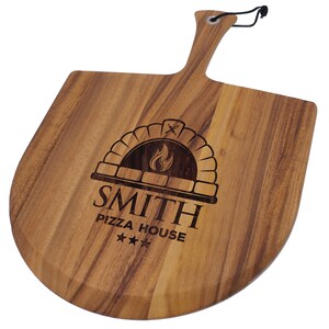 Peut inclure: Une pelle &agrave; pizza en bois avec une poign&eacute;e et une lame incurv&eacute;e. La pelle pr&eacute;sente un motif grav&eacute; au laser d'un four &agrave; pizza avec une flamme, les mots "SMITH PIZZA HOUSE" et trois &eacute;toiles.
