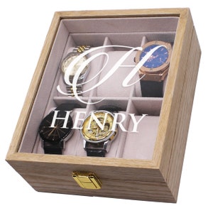 May include: A wooden watch box with a glass top, containing four watches. The box is engraved with the name "HENRY" and a large letter "A". The watches have various band and face colors, including gold, silver, black, and blue.