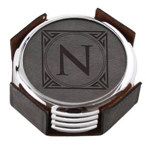 May include: Set of four gray leather coasters with a silver metal rim. The coasters feature a silver metal frame with an engraved letter "N" in the center.